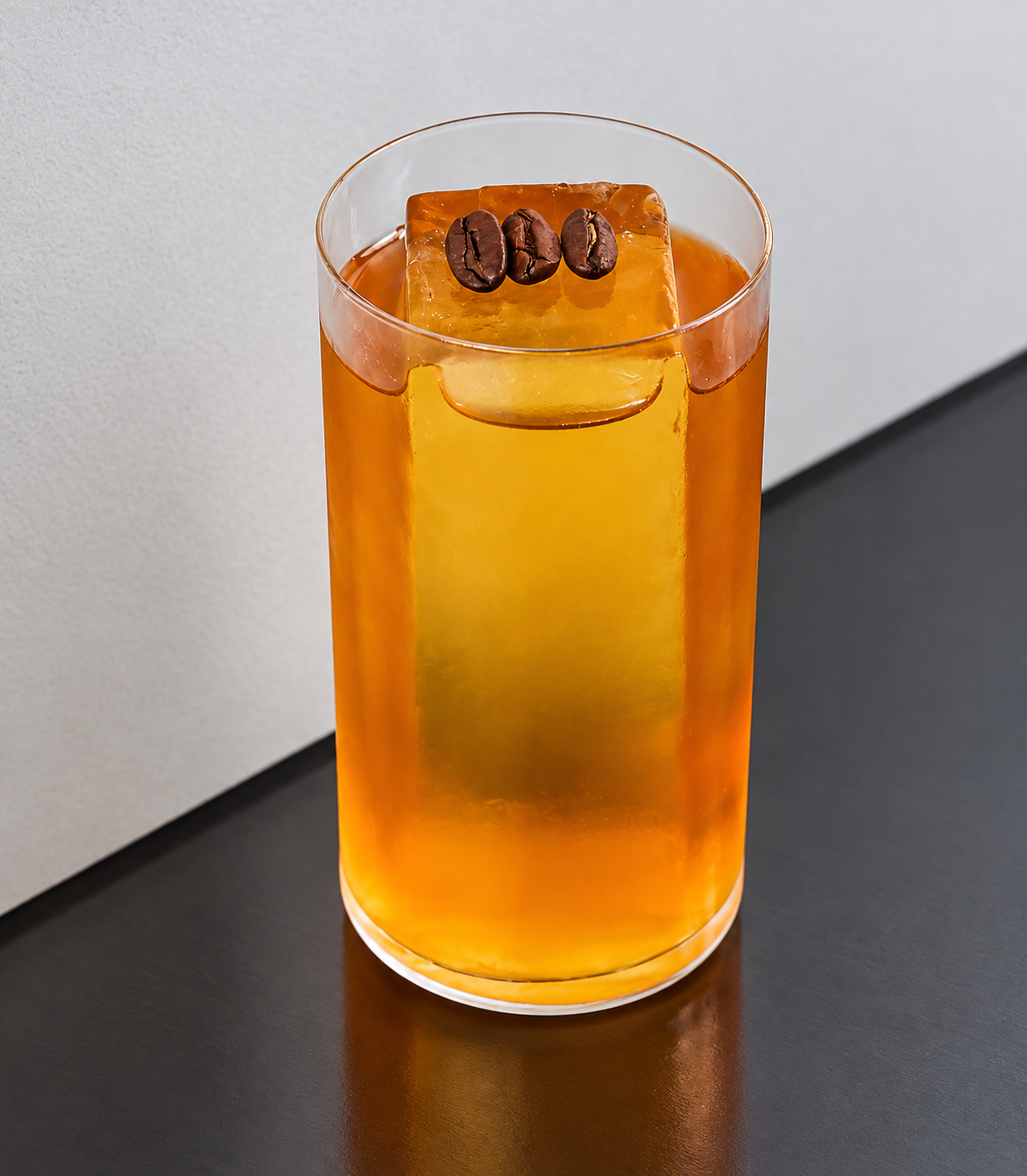 Golden amber cocktail with a clear ice block and three coffee beans