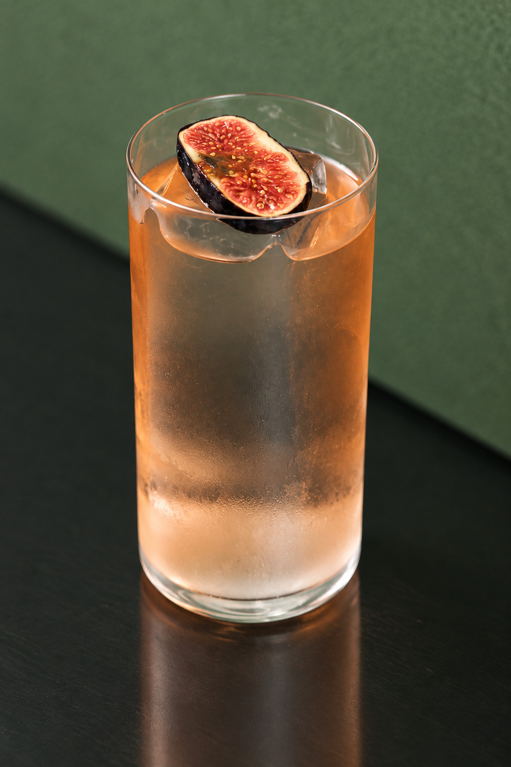 Amber cocktail with a fresh fig garnish against a green backdrop